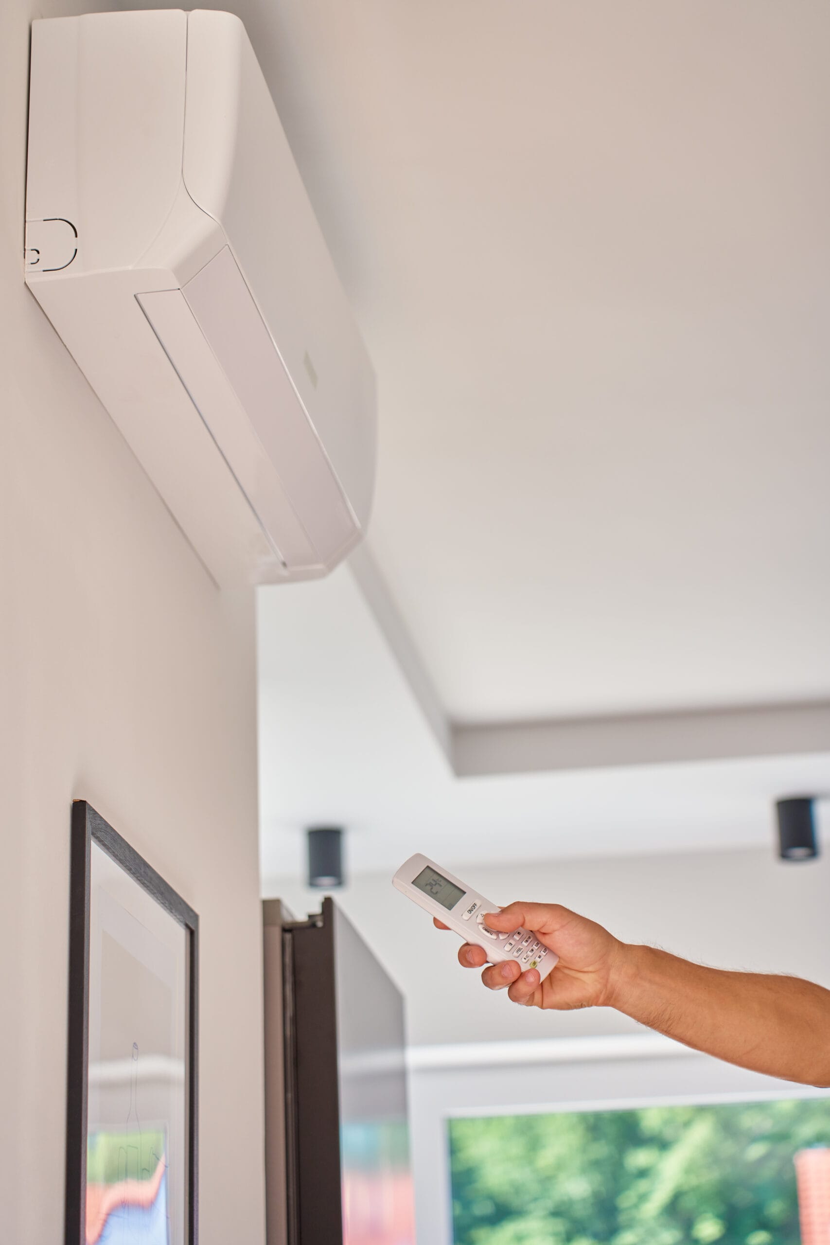 Hand using remote control to adjust temperature on air conditioner at home